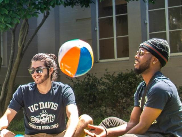Students sit outside with beach ball during the summer.