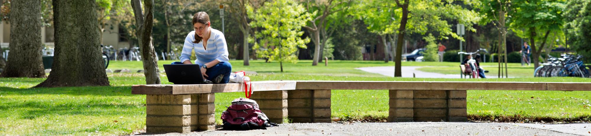 Student using computer on a bench in the quad.