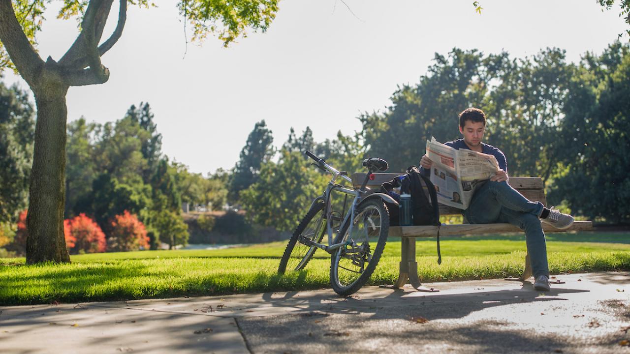 Student reading newspaper in arboretum.