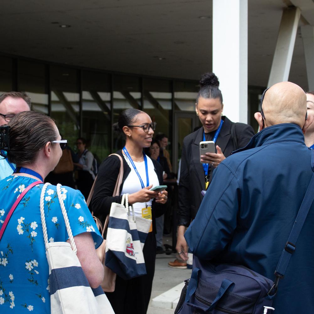 Group of conferencegoers contemplating plans standing in a circle outside.