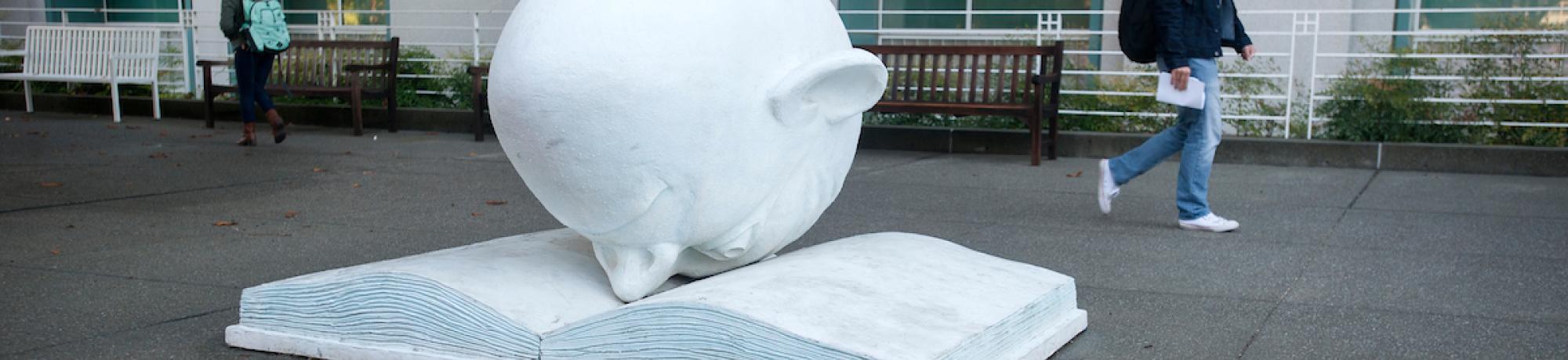 Egghead sculpture with nose in book.